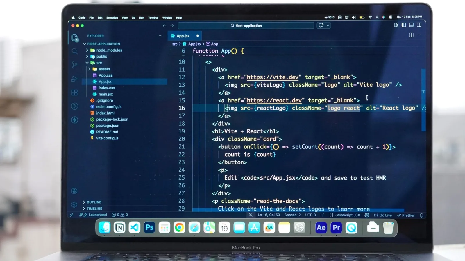 A laptop screen showing React code editor with TypeScript syntax highlighting